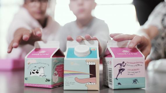 I forgrunnen tre skolemelk-kartonger, i bakgrunnen tre elever som strekker hendene mot kartongene